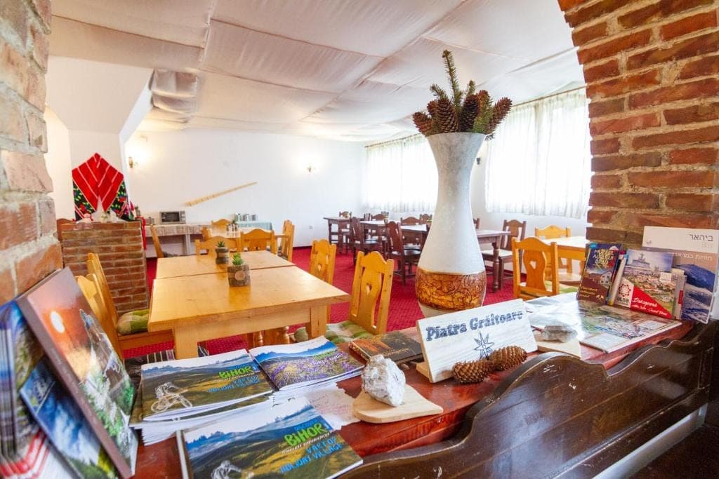 Sala de mese văzută prin arcada din cărămidă, cu o vază cu conuri de brad și pliante despre zonă