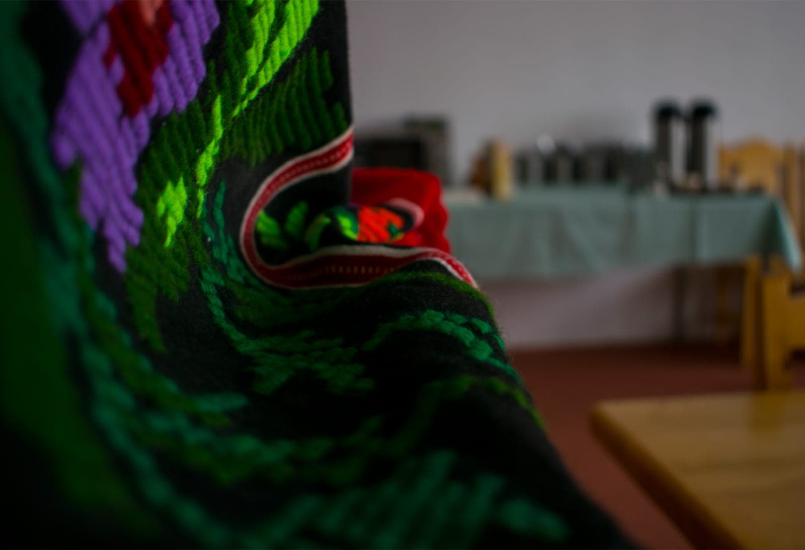 Țesătură tradițională cusută în verde și mov, cu sala de mese în fundal