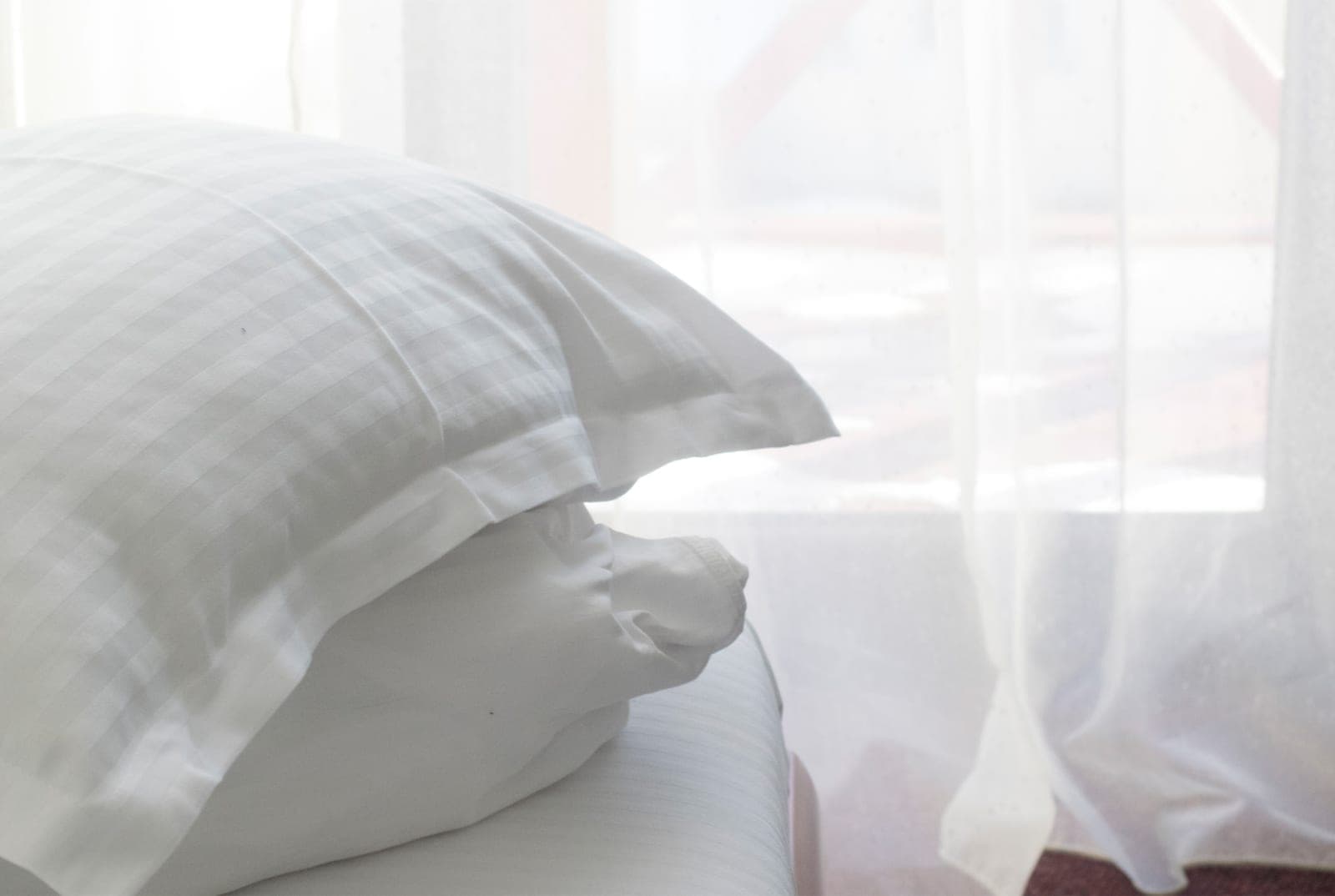 White pillows on the bed, in the light of a curtained window