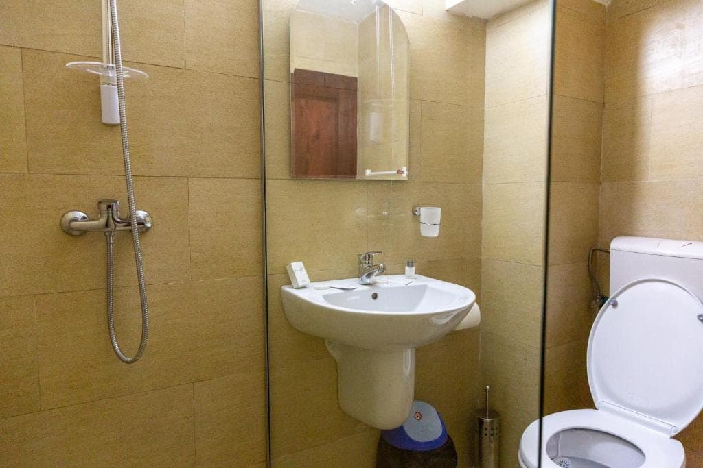 A bathroom with beige tiles, a glass-walled shower, a washbasin and a mirror