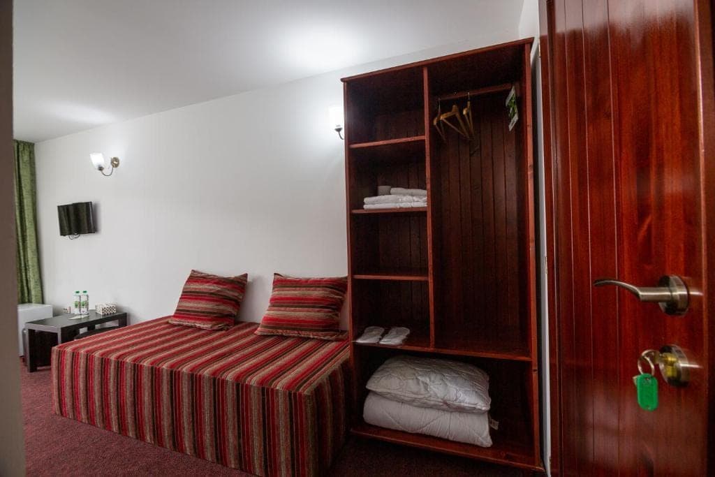 A room with a red-striped bedspread, an open wooden wardrobe and the wooden door