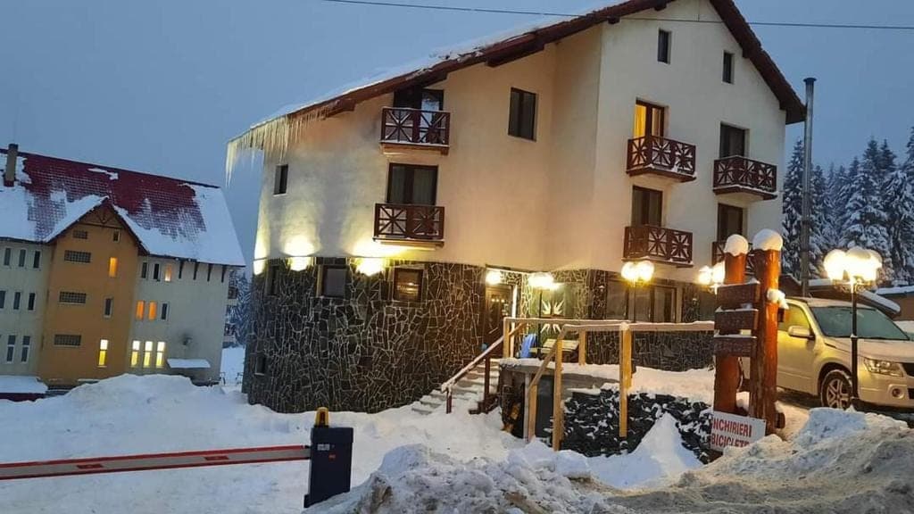 Pensiunea iarna, seara, cu luminile aprinse pe soclul de piatră și balcoane